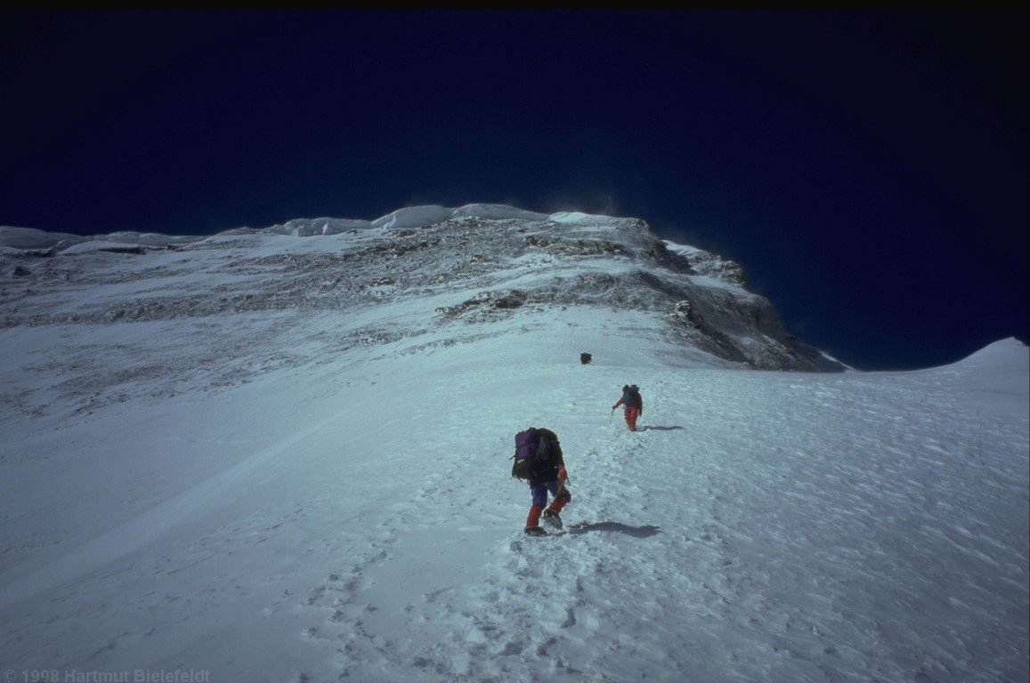The snow slope ends in a steep rock wall.